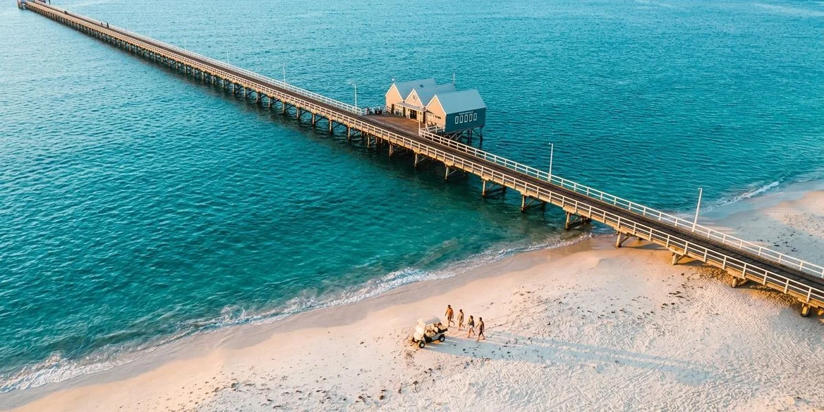 Aerial view of the iconic Busselton Jetty stretching into turquoise Geographe Bay waters with white sand beach and coastal town behind