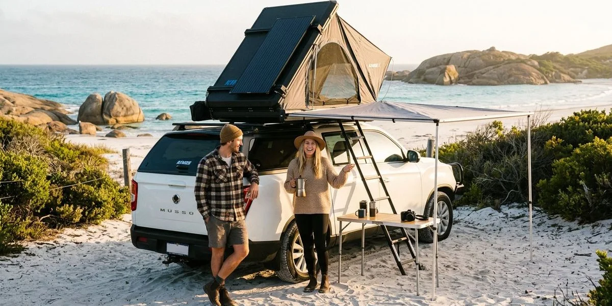 Happy couple standing beside their fully equipped 4WD camper at a scenic Western Australian coastal campsite at golden hour