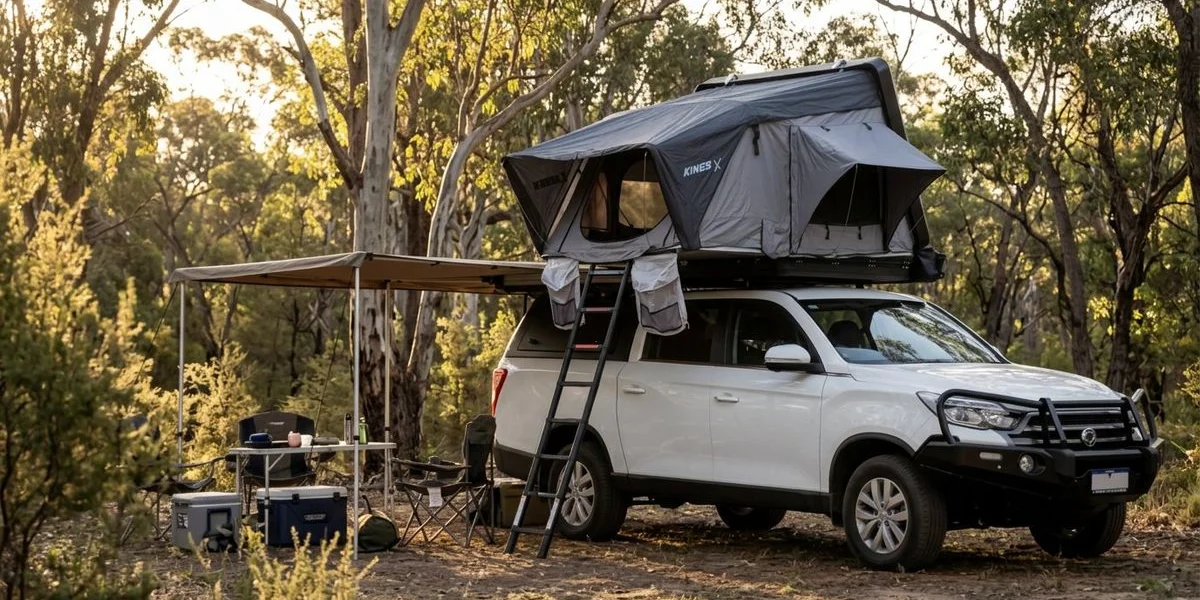 A spacious campsite setup with a dual-cab 4WD camper showing deployed awning camp table and chairs with bushland in the background
